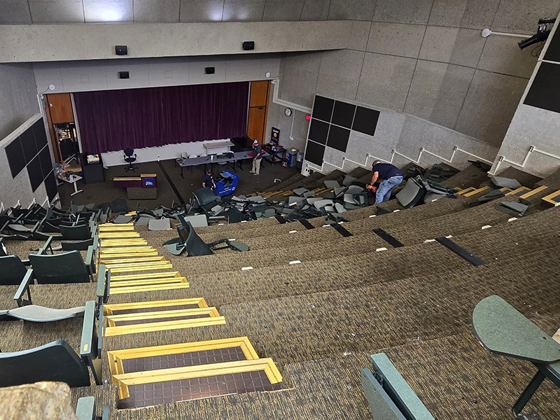 Disassembled seating in a large lecture hall, with debris scattered across the floor.