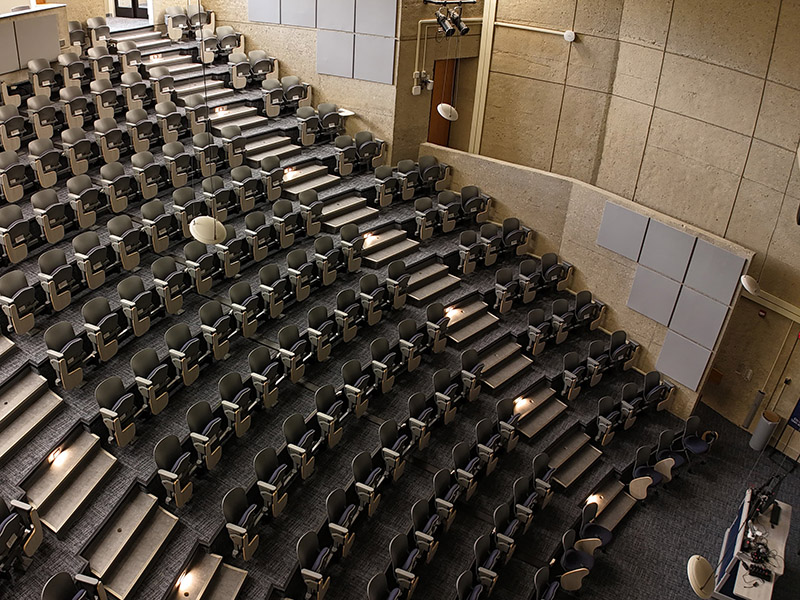 Tiered lecture hall with gray seats and concrete walls.