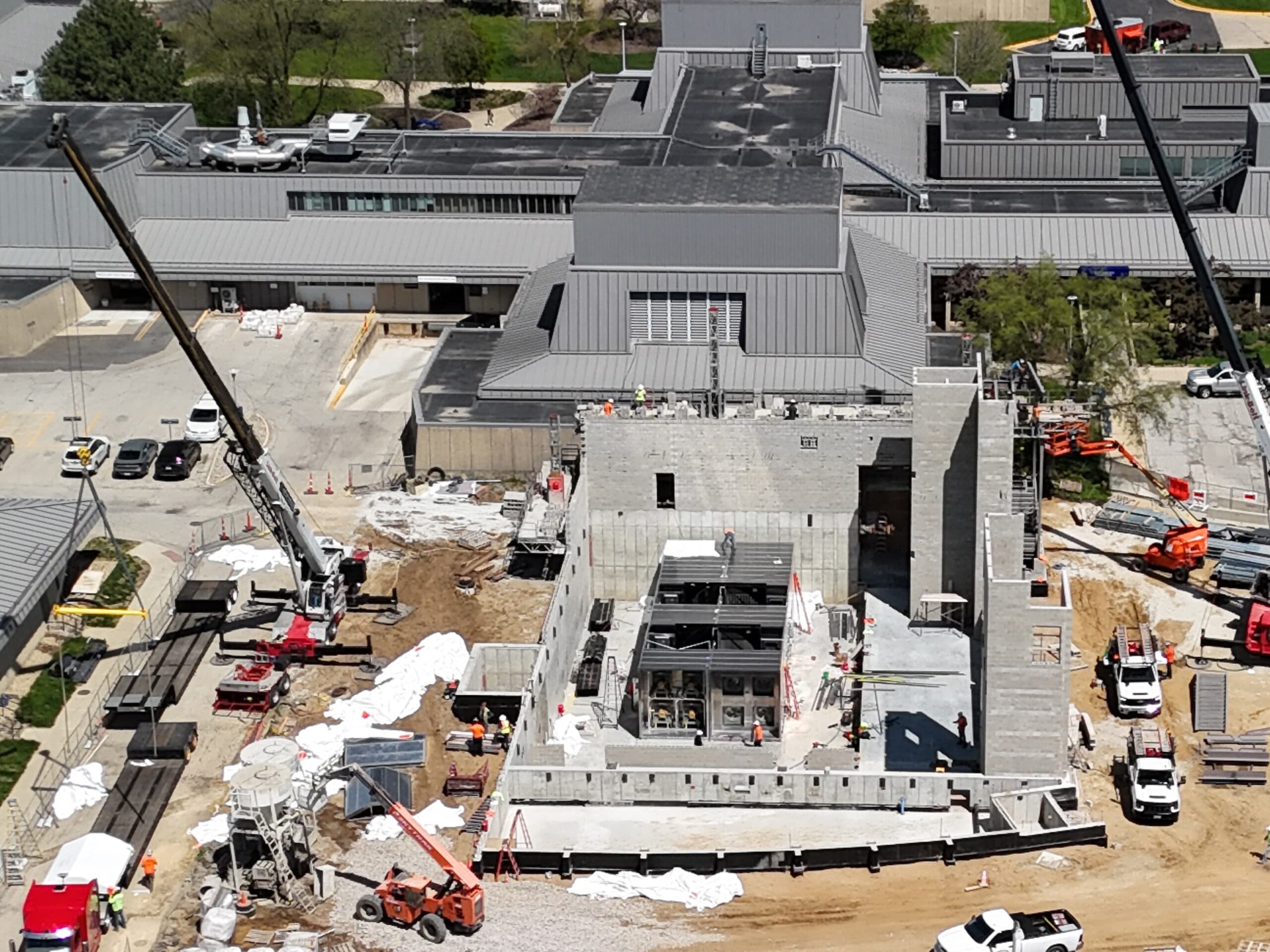 Aerial view of a construction site with cranes, vehicles, and workers next to a large modern building complex.