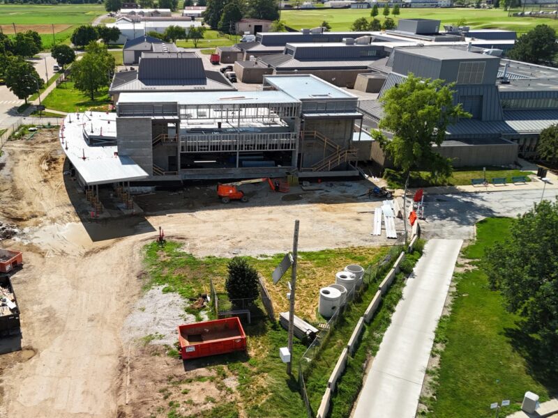 Aerial view of a large construction site with a partially built building, surrounded by dirt, construction materials, and vehicles.