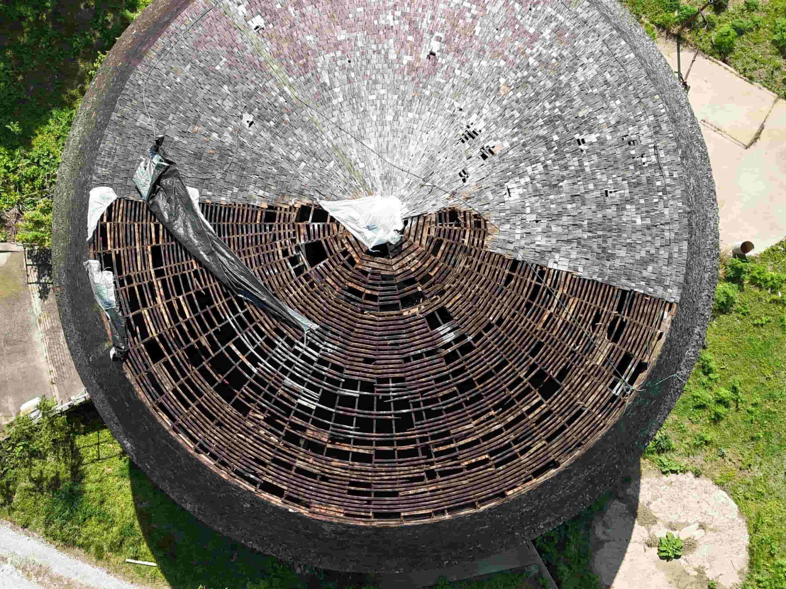 Aerial view of a round barn with the roof partially removed, exposing wooden framing during restoration.