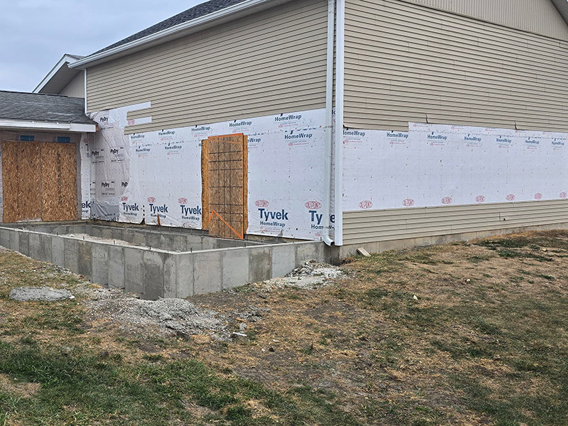 Exterior view of the Wildlife Medical Clinic Education Center under construction at the University of Illinois College of Veterinary Medicine. The image shows a building with new siding, Tyvek house wrap, and framed openings for doors, along with a concrete foundation for an upcoming addition.