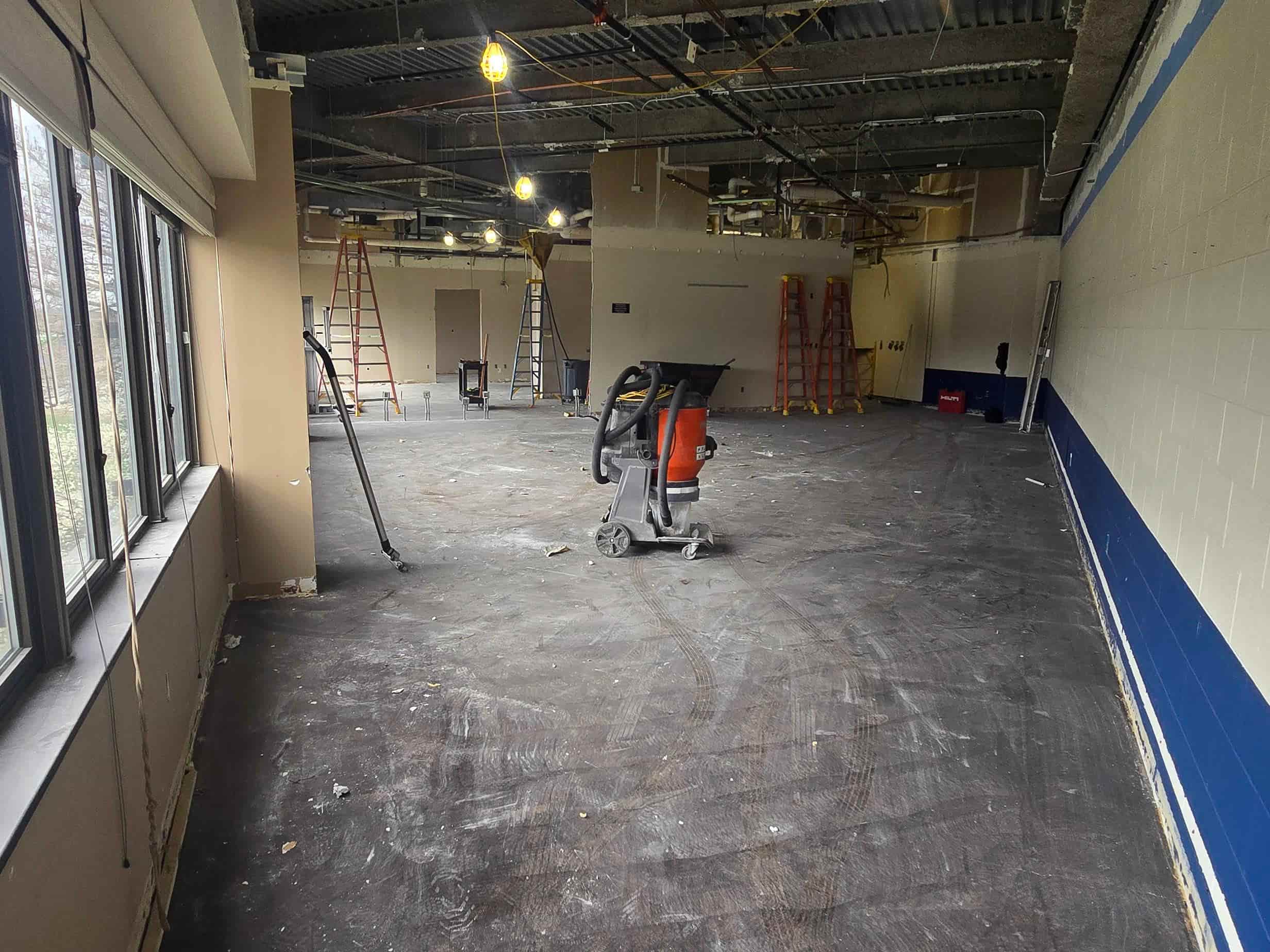 Interior space under renovation with open ceilings, ladders, construction equipment, and demolition tools on the floor.