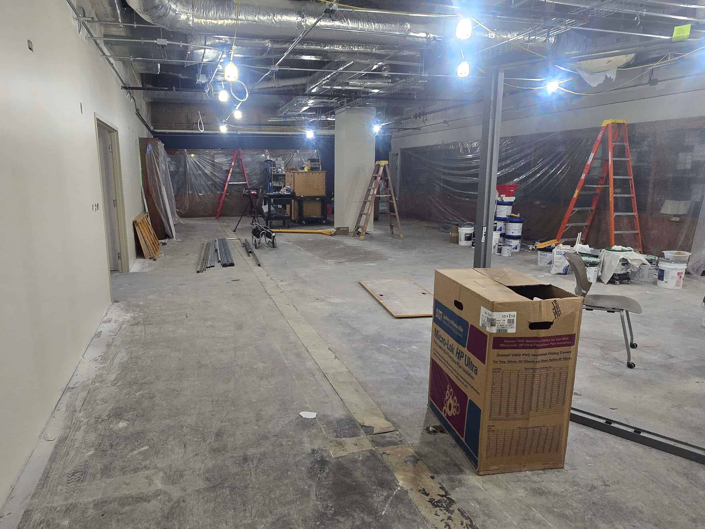 Finished interior under renovation with exposed ceiling, ladders, plastic sheeting, and construction materials.