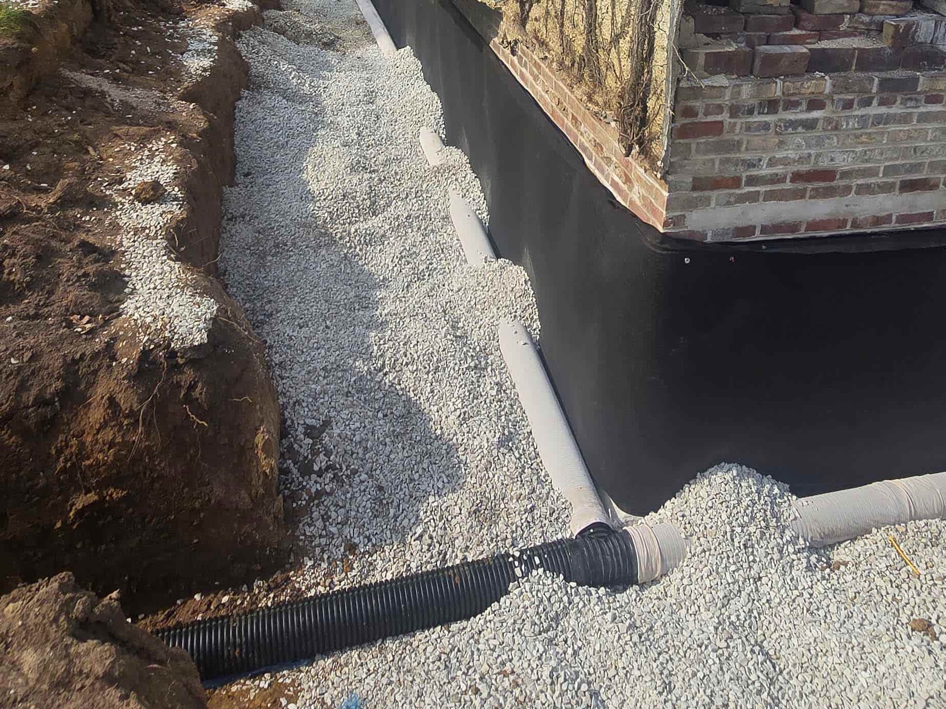 Foundation drainage system installation with waterproofed foundation wall, drain tile, and drainage stone at the Manager House.