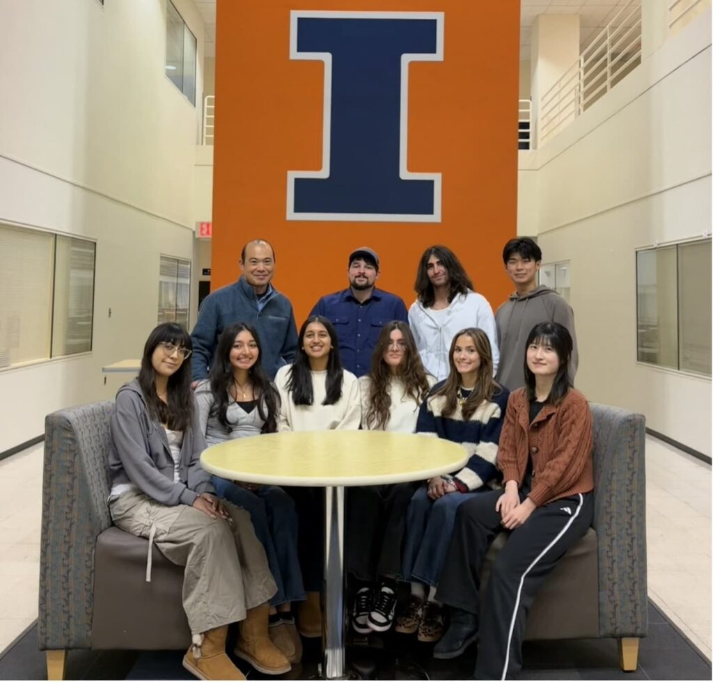 Dr. Inoue’s lab team of ten members stands together in front of the large Block I installation in the atrium of the Basic Science Building at the College of Veterinary Medicine.
