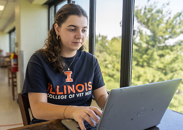 student sitting next to a window typing on a laptop computer 