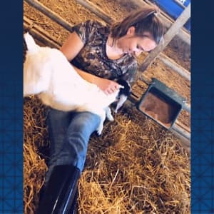 Alicyn Tilk in barn sitting holding a goat