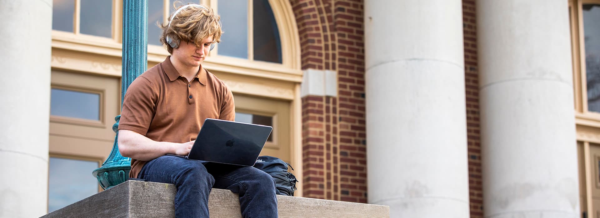 Student looking at laptop outside of building.