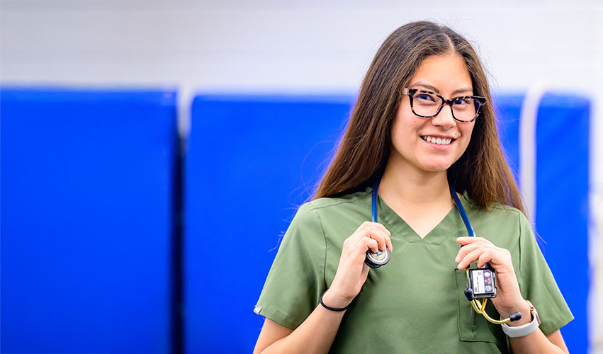 Young women in greens scrubs holding her stethoscope and smiling