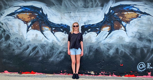 [Sara Colin poses in front of a mural of a bat]