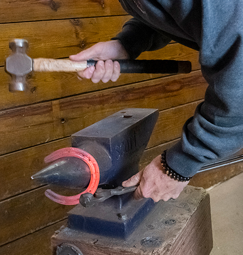a farrier hammers a red-hot horseshoe