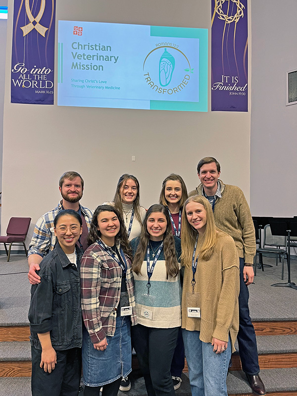 eight Illinois veterinary students pose in front of banner for Christian conference
