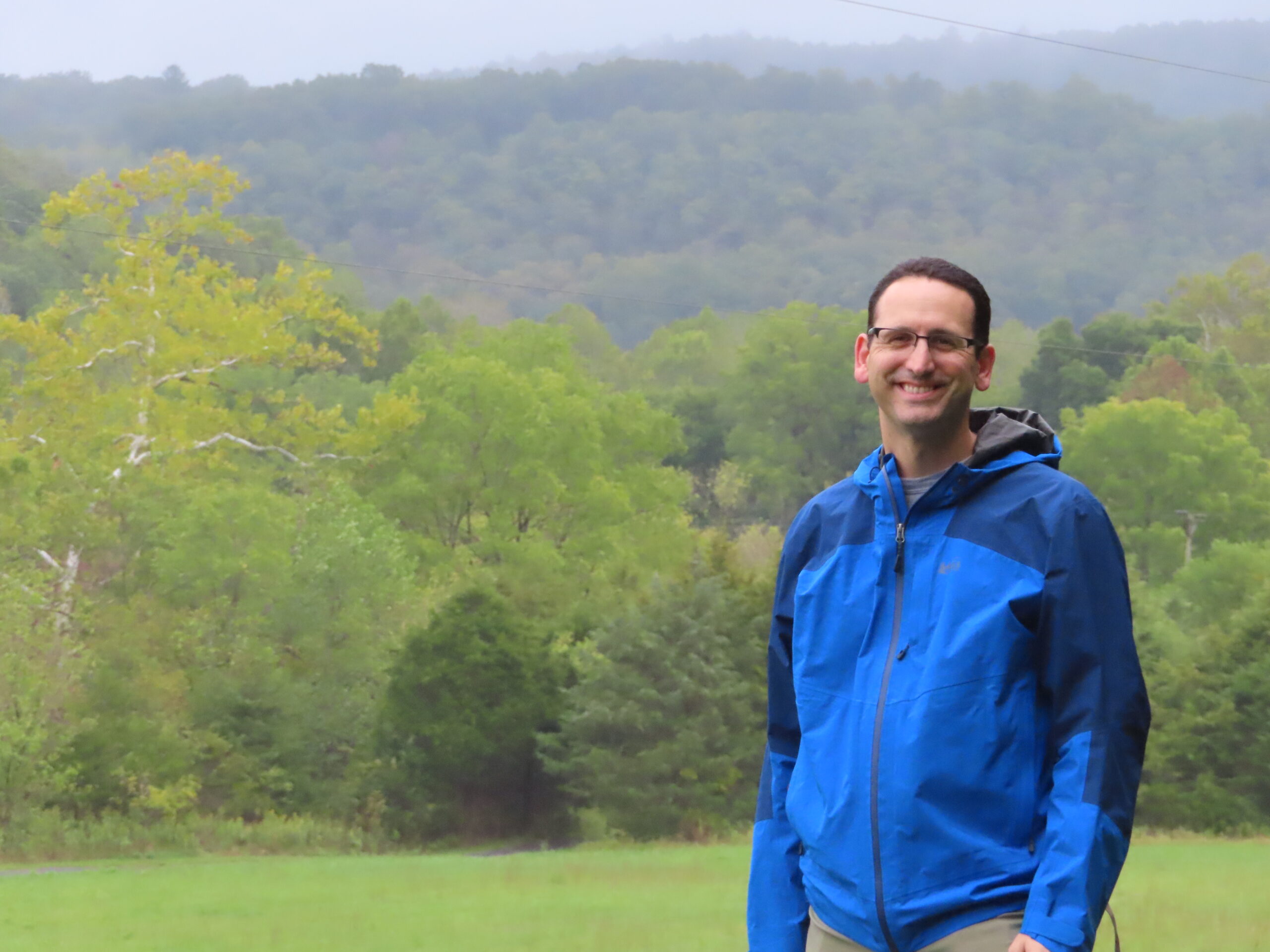 Jeff Fox standing in front of a grass field and forest.