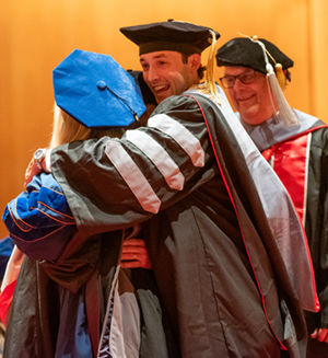 Class of 2024 DVM graduate, Dr. Grace Steinman, receives a group hug by veterinarian father and brother, while her grandfather looks on during the convocation ceremony.
