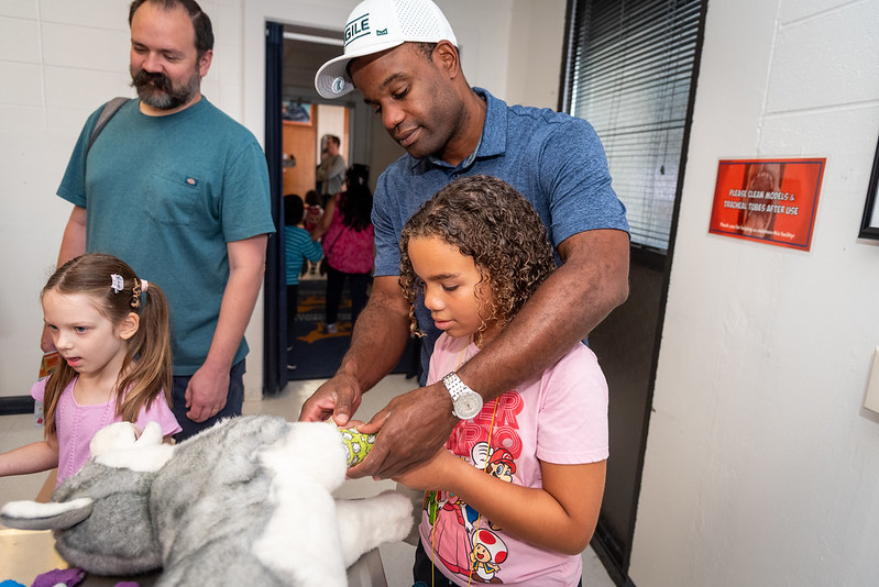 A father and daughter learn how to put a cast on a toy dog at Open House 2024.