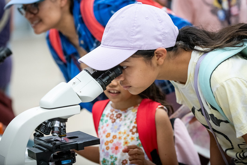 Two girls look through a microscope at Open House 2024.