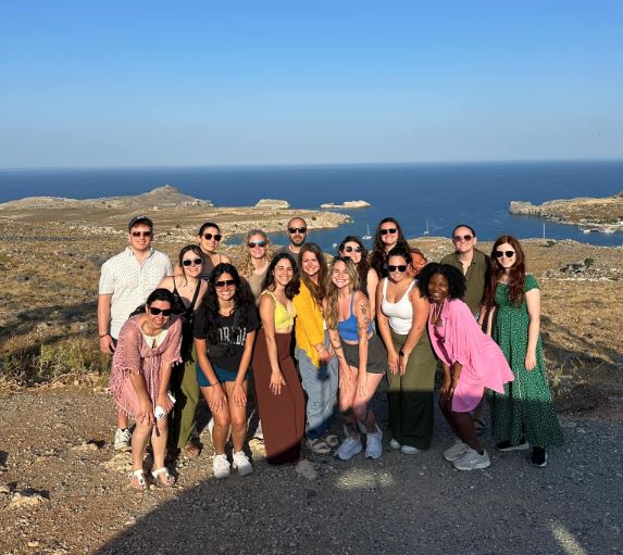 A group of student veterinarians pose and smile in front of a body of water.