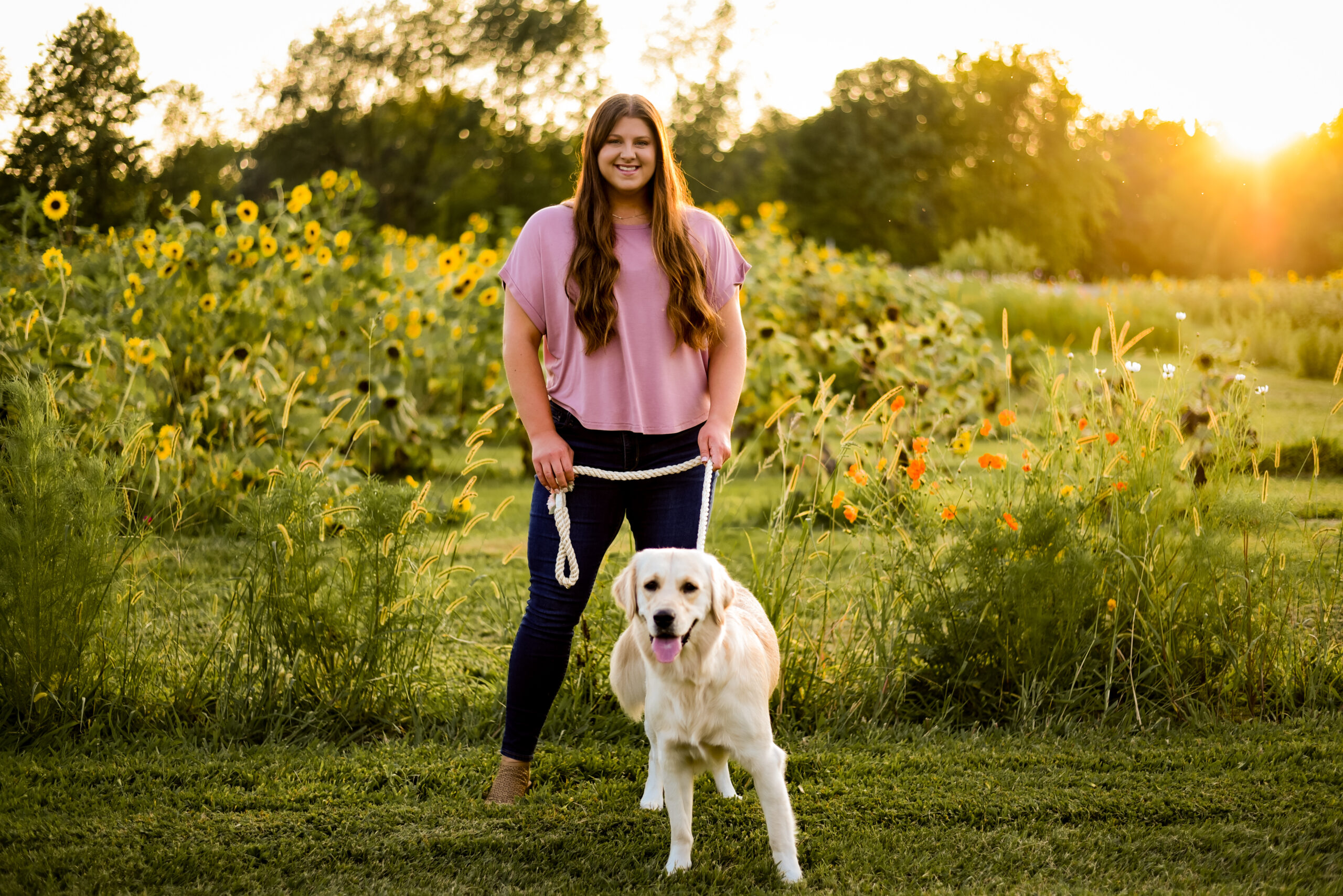 Caitlin Acree standing in a field with her golden retriever, Luna, on a rope leash.