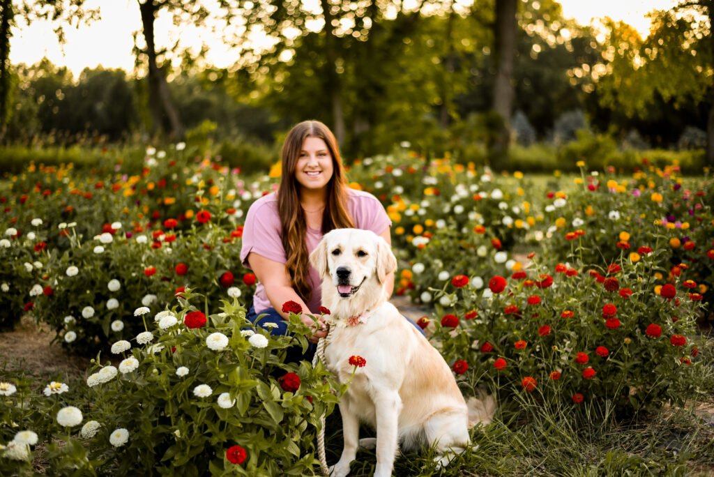 Caitlin Acree sitting in a field of flowers with her golden retriever, Luna.