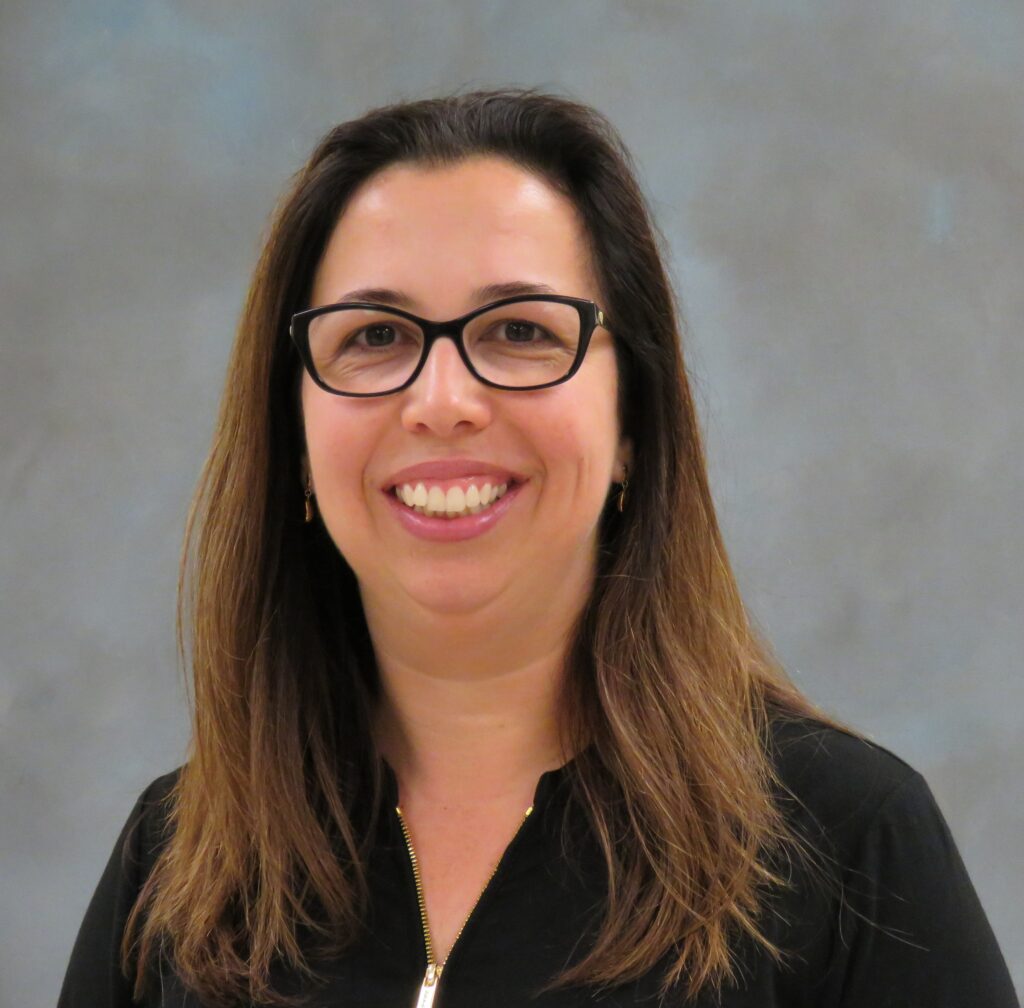 Dr. Clarissa Souza smiles in front of a gray backdrop.