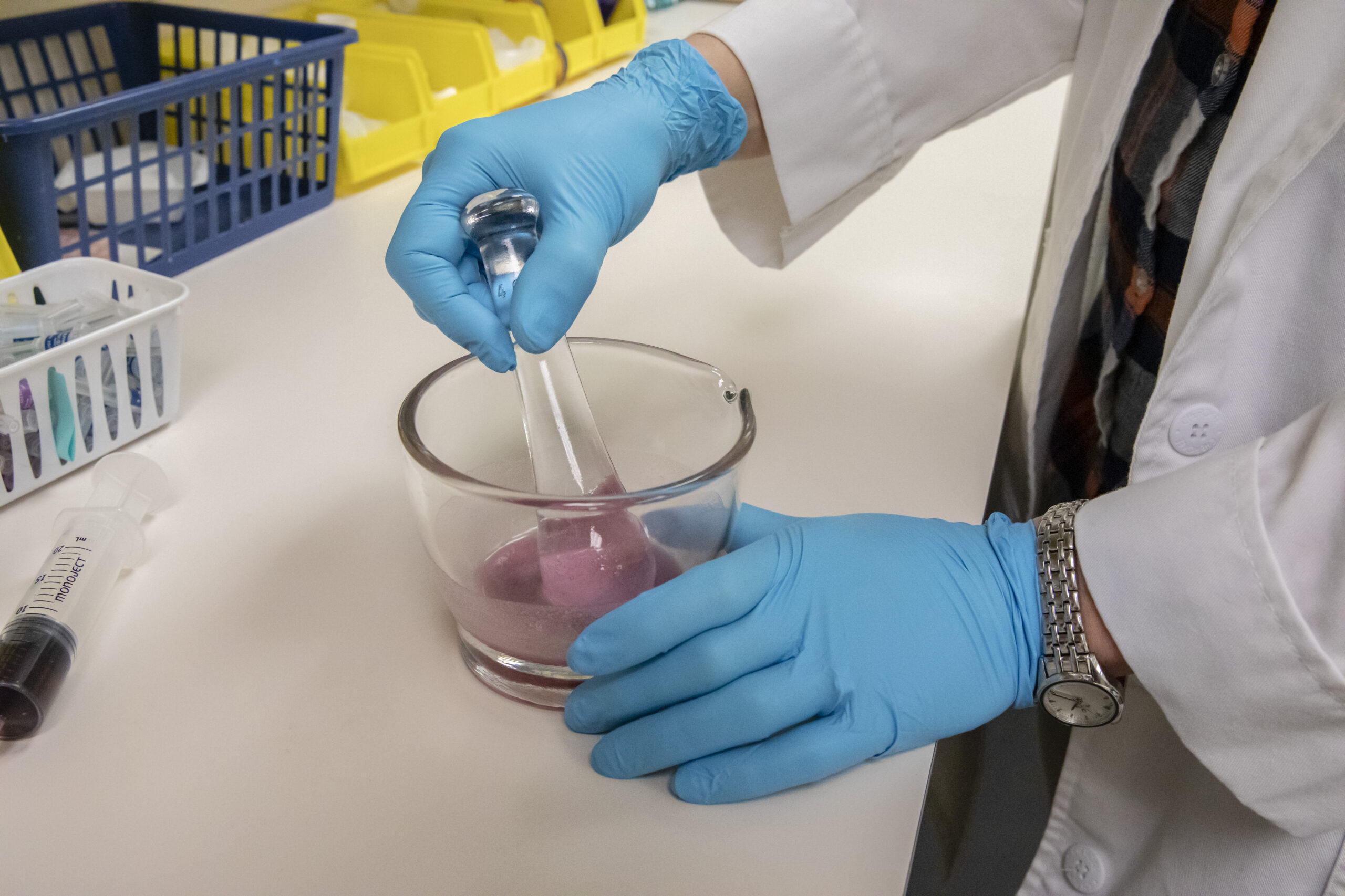 A pharmacist mixing a pink liquid while wearing blue gloves.