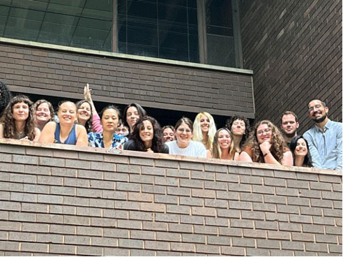 Seventeen students and staff of the institute look over a brick terrace at the Levis Faculty Center to pose for a group photo.