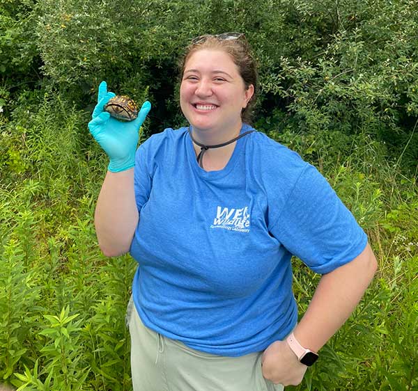 Student Kelly Giles smiles and holds up an Eastern Box Turtle in her right hand that has a turquoise surgical glove on it.