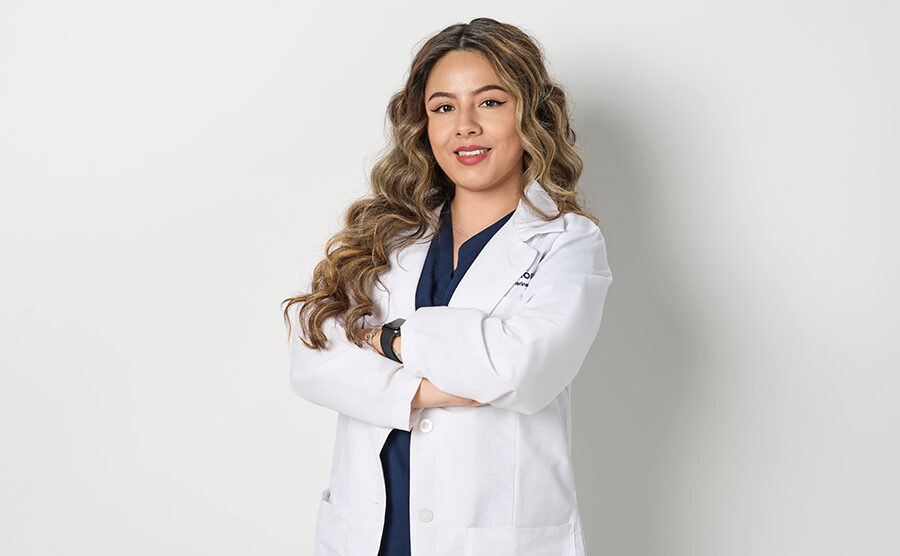 A veterinarian posing with their arms crossed and white coat on in front of a white background.