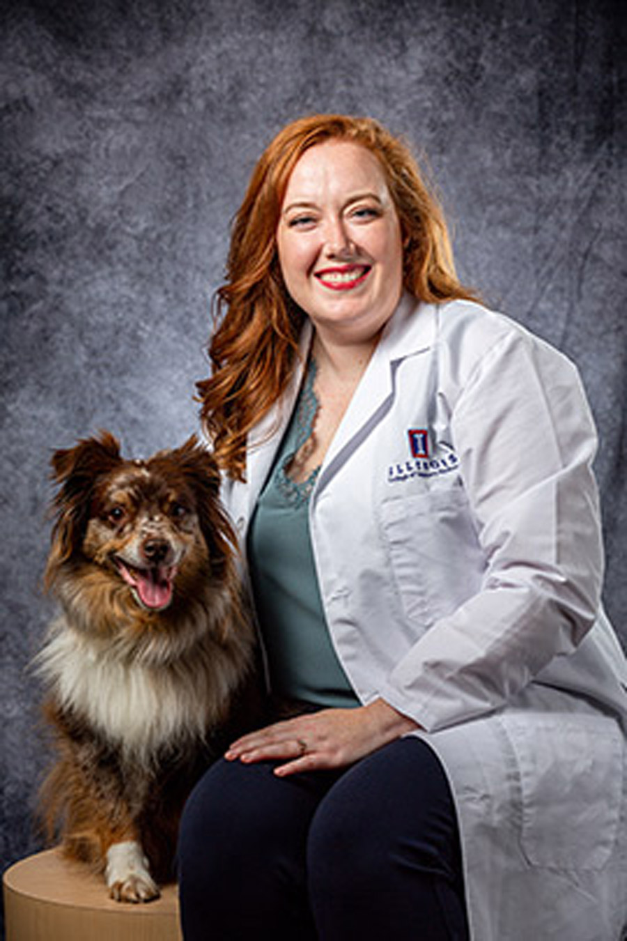 A veterinarian and dog smiling in front of a gray background.