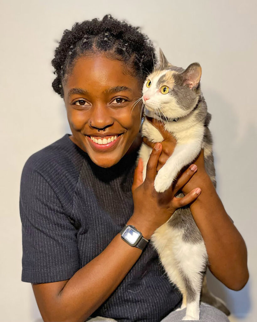 OC Kirkland smiling with a gray and white cat in front of a white wall.