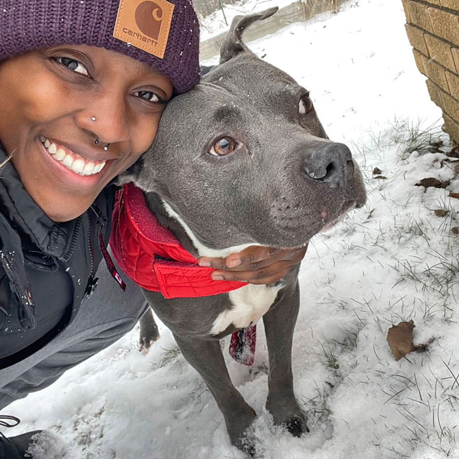 OC Kirkland posing with a gray dog in a red vest outside during the winter season.