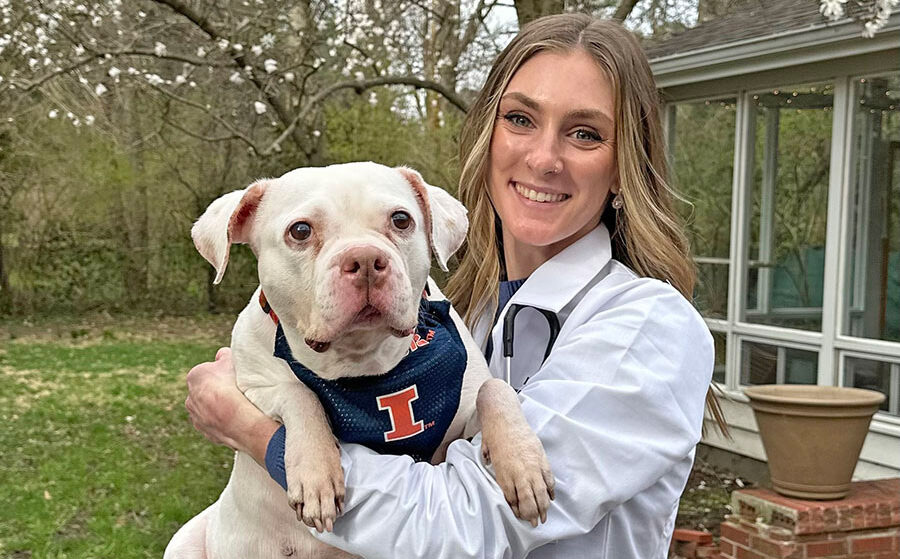 A veterinarian in a white lab coat holding a dog with a University of Illinois bandana.