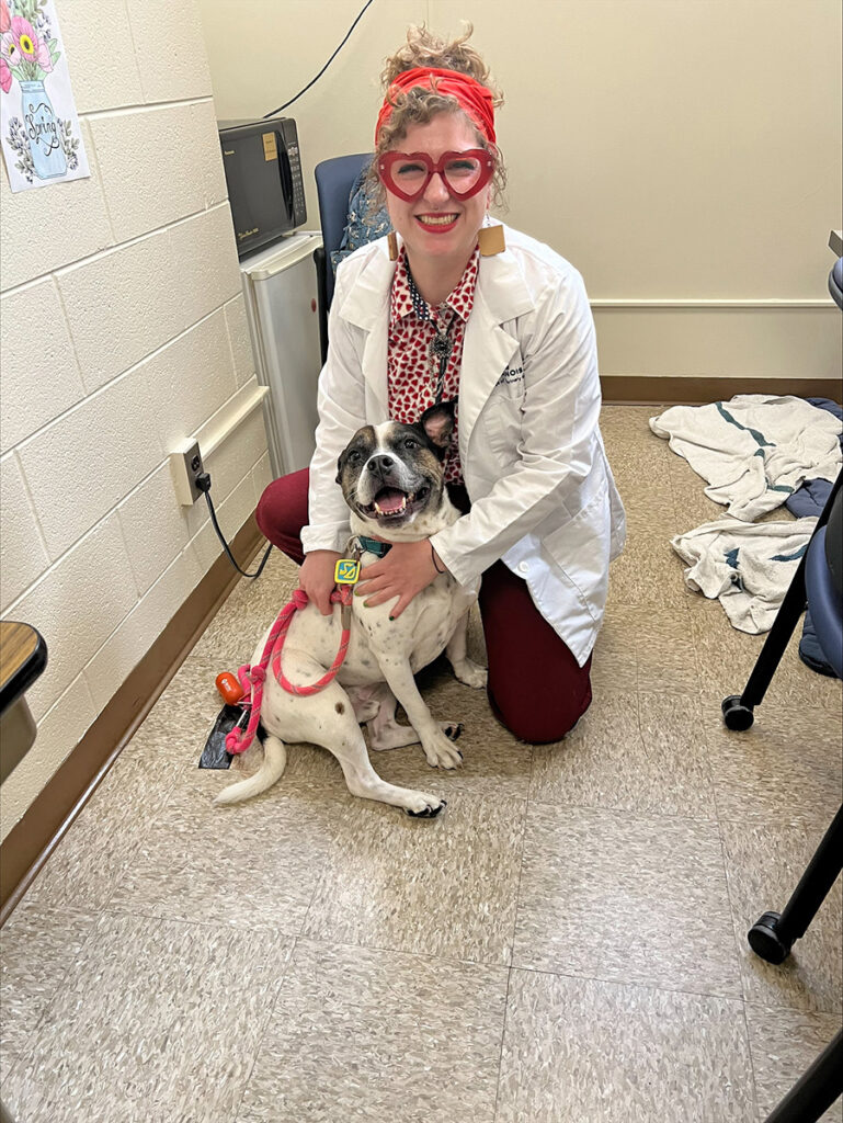 Kristine Witte holding onto the leash of a dog and smiling with the dog for the photo.