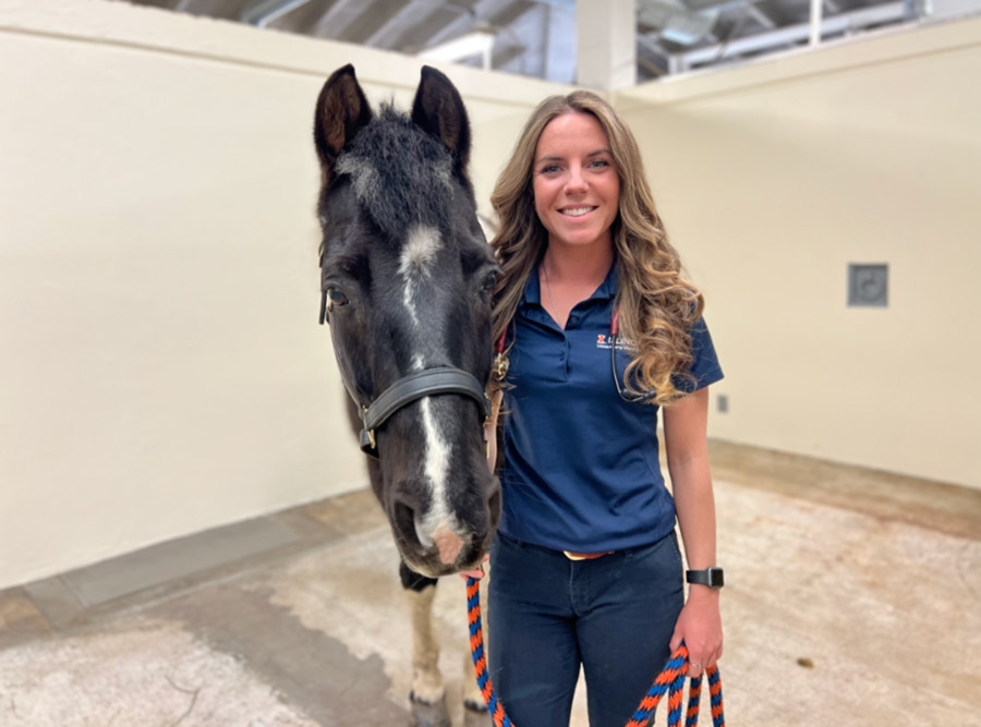 Gina Kowalewicz posing alongside a black and white horse.