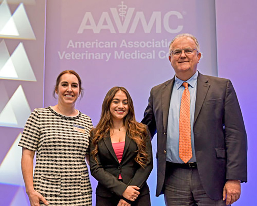 Naomi Esquivel in the middle of Drs. Peter Constable and Sandra Faeh Butler in front of a sign that reads "American Association of Veterinary Medical Colleges."