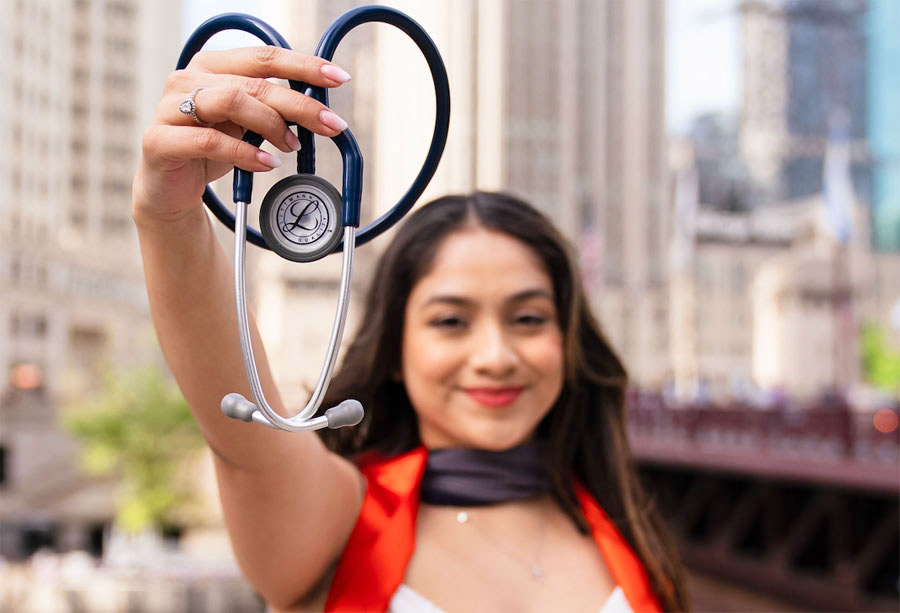 Naomi Esquivel holding up a stethoscope with her and a city in the background blurred.