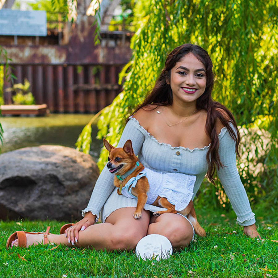 Naomi Esquivel and her Pomeranian-chihuahua Petunia posing on the grass in front of a lake,