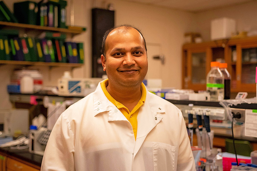 Dr. Ratnakar Singh smiling in a white lab coat in an office setting