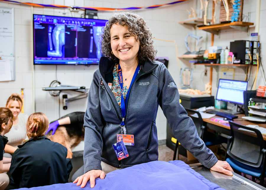 Dr. Caroline Garzotto poses in the orthopedic surgery exam room with students, a dog, radiographs, and a skeleton behind her