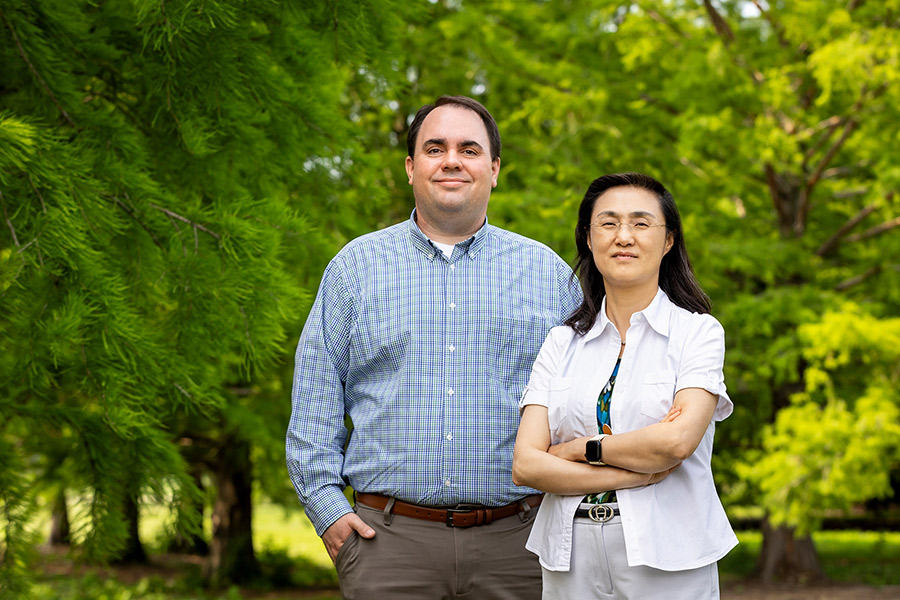 Drs. Christopher Gaulke and Ying Fang posing outdoors near several trees, both smiling.