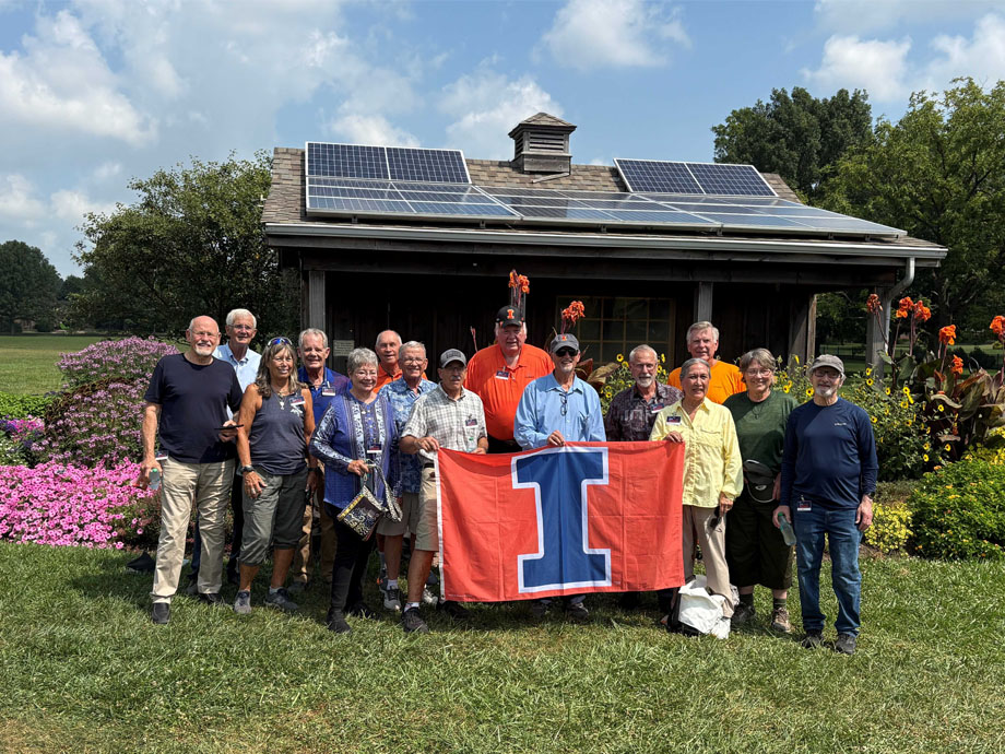 Class of 1975 alumni reunion posed with the Block I flag in front of a building with summer flowers in full bloom