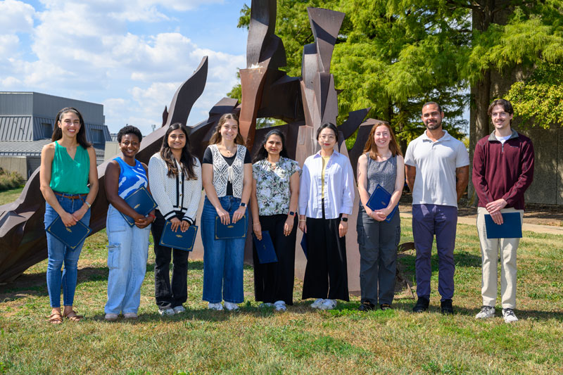 Pthobiology graduate students pose in front of a College of Veterinary Medicine sculpture