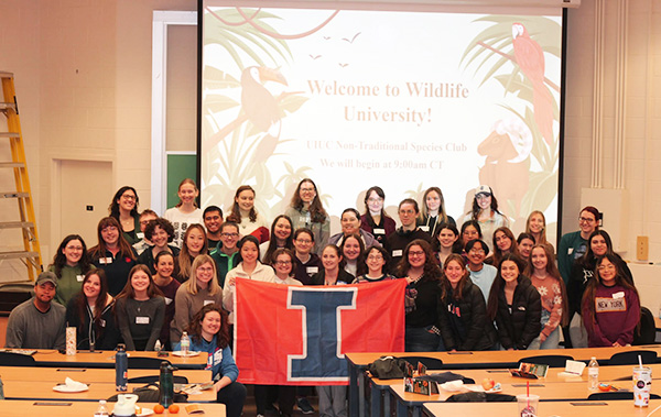 Group holding an orange flag with a blue block I during Wildlife University